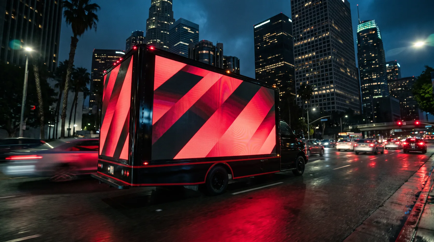 LED billboard truck glowing red on rain-slicked pavement against the Downtown Los Angeles skyline at night